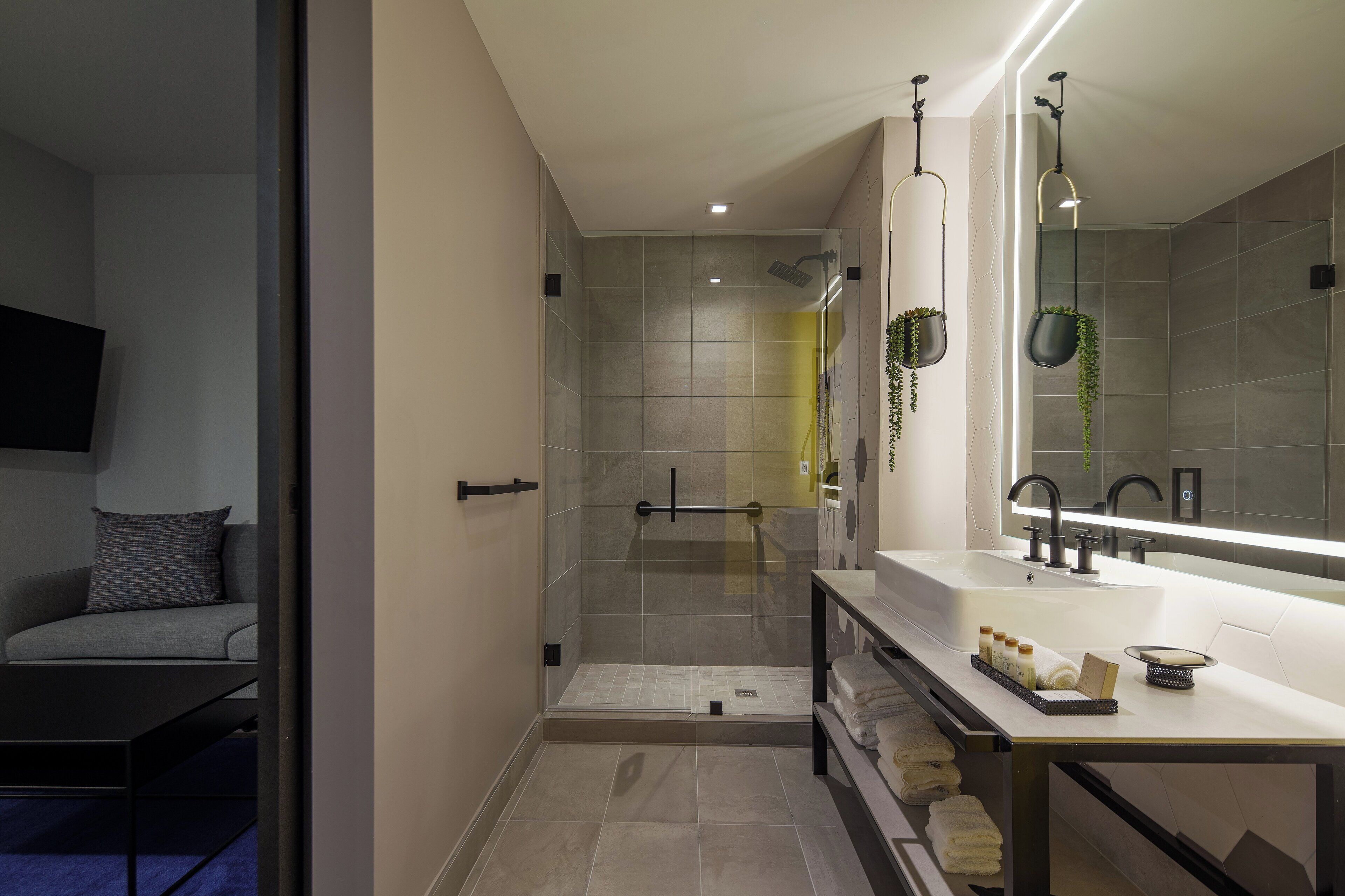 A modern bathroom with a glass-enclosed shower, a large mirror, and a vanity with towels.