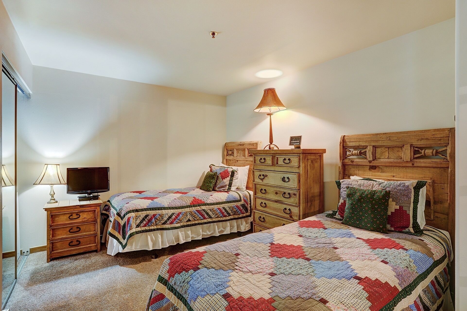 A bedroom with two beds, a dresser, a TV, and a lamp.