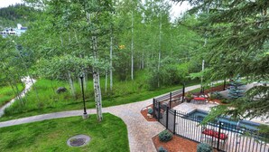 A landscaped outdoor area with a paved walkway, a seating area with a table and chairs, and a fenced garden with various plants and trees. - Newly Renovated 2 Bed/ 2 Bath Beaver Creek  2 Bedroom Condo by RedAwning (Avon)