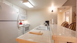 A compact kitchen with white cabinets, a refrigerator, a microwave, a stove, and a sink. - Nine Vail Road Condos in Heart of Vail Village by RedAwning (Vail)