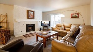 A living room with a fireplace, leather sofa, and a television. - Nine Vail Road Condos in Heart of Vail Village by RedAwning (Vail)