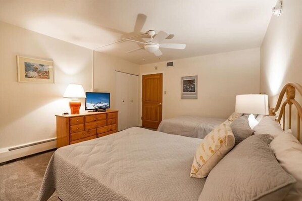 Une chambre à coucher avec un lit, deux tables de chevet, un ventilateur de plafond, une télévision et une porte.