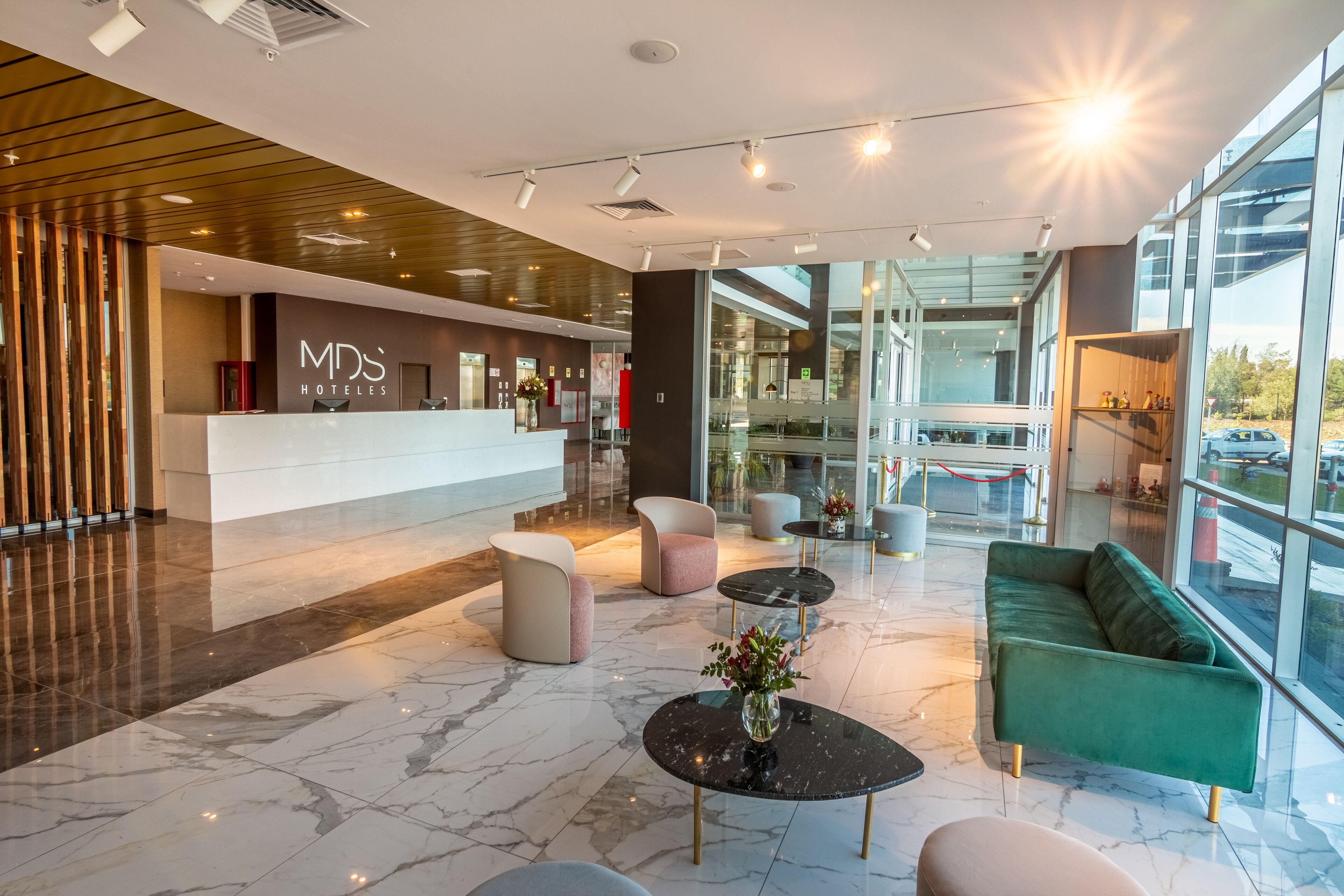 A modern hotel lobby with a reception desk, plush seating, and large windows offering views of the outside.