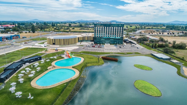 Un hôtel moderne doté d’une cour intérieure où se trouvent deux piscines, un espace de jeux pour enfants et un grand bâtiment à la façade en verre.
