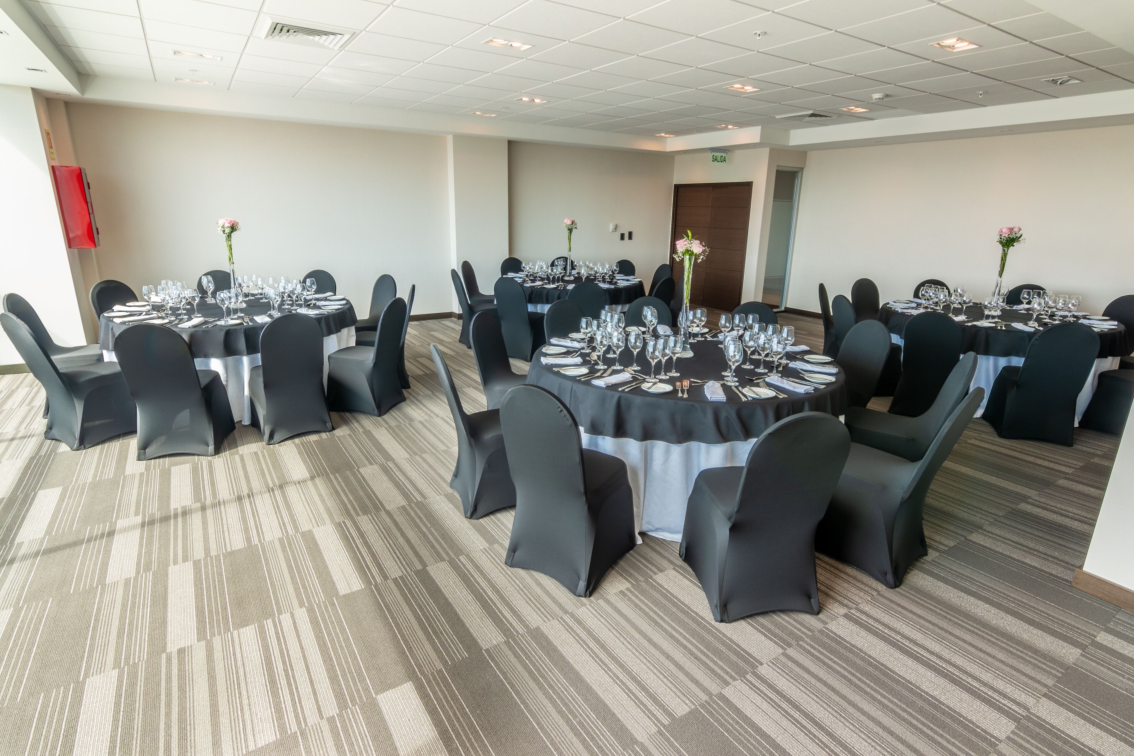 Un salón de conferencias con mesas redondas, sillas negras y centros de mesa con flores.