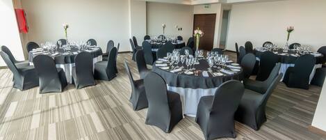 Un salón de conferencias con mesas redondas, sillas negras y centros de mesa con flores.