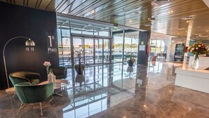 Un hall d’entrée moderne avec une entrée en verre, un comptoir d’accueil et un fauteuil vert.