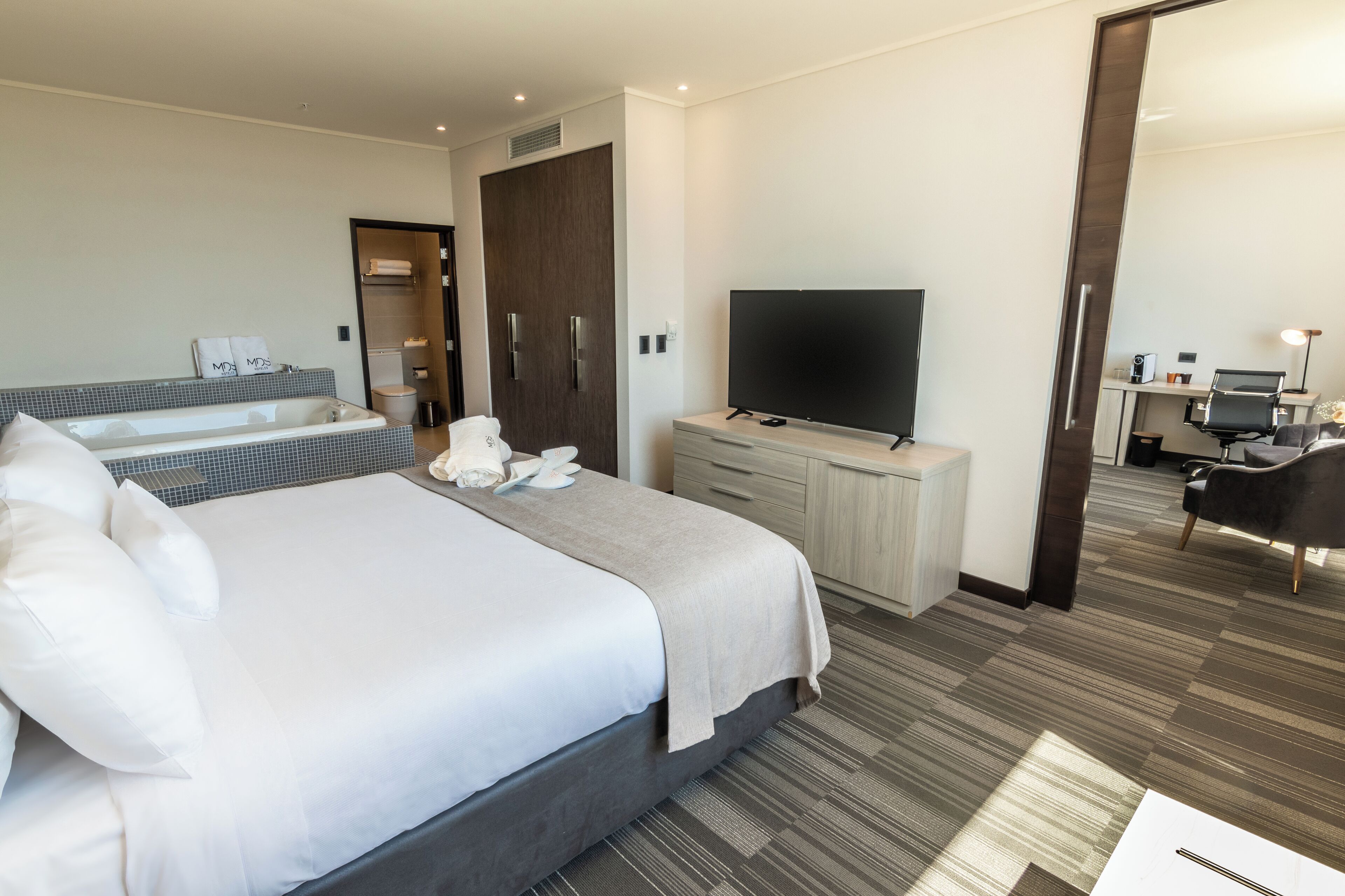 Una habitación de hotel moderna con una cama grande, un televisor de pantalla plana, un escritorio con computadora y un baño con bañera y inodoro.