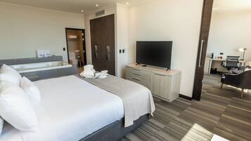 Una habitación de hotel moderna con una cama grande, un televisor de pantalla plana, un escritorio con computadora y un baño con bañera y inodoro.