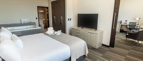 Una habitación de hotel moderna con una cama grande, un televisor de pantalla plana, un escritorio con computadora y un baño con bañera y inodoro.