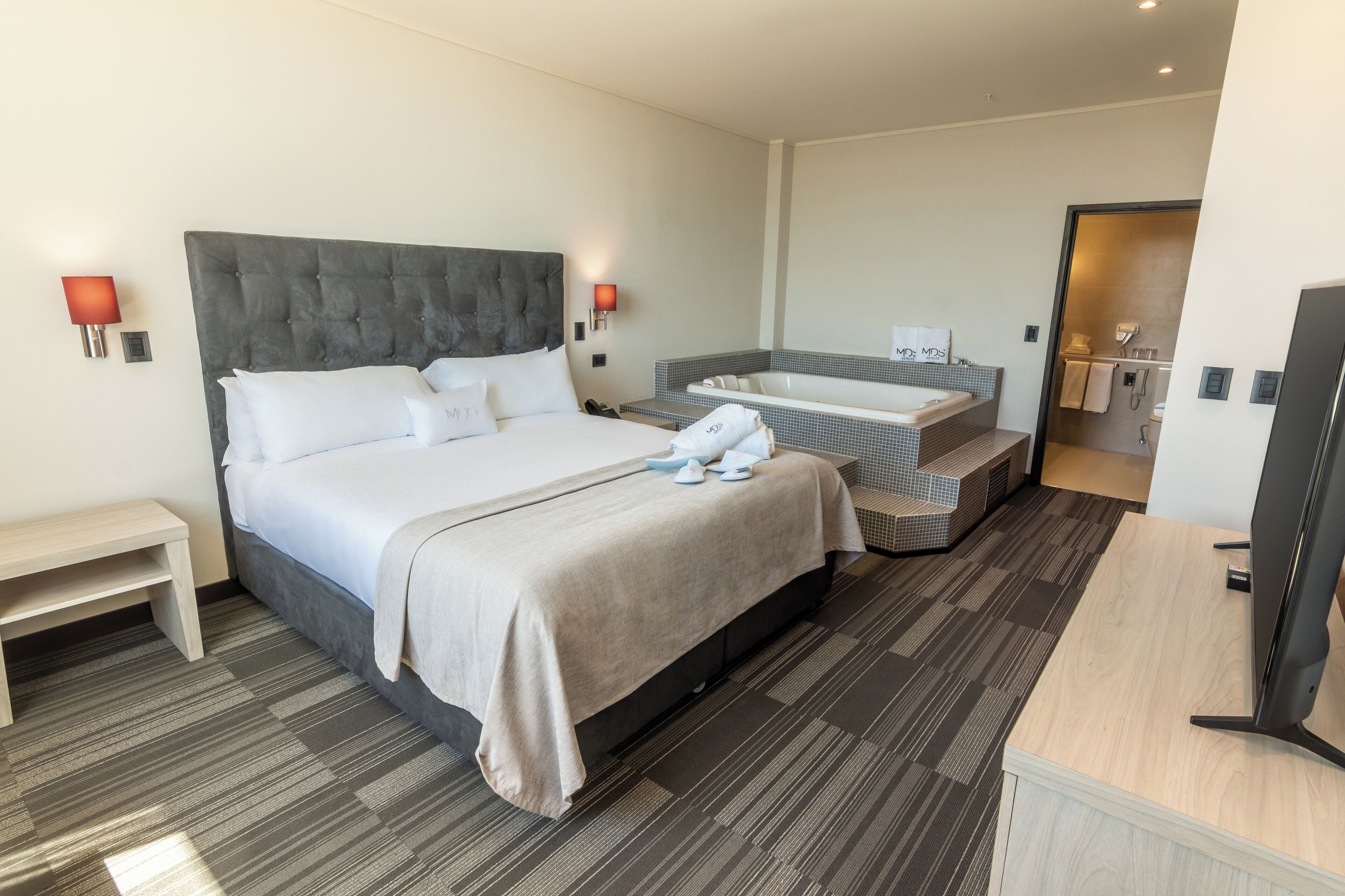 A hotel room with a large bed, a small desk, a TV, a bathroom with a bathtub, and a shower.