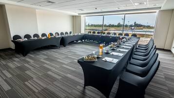 Un salón de conferencias con una larga mesa, sillas negras y vistas a un viñedo a través de amplias ventanas.
