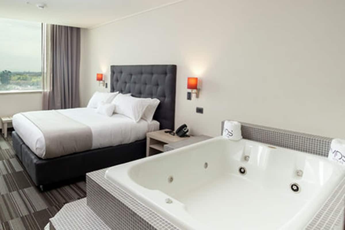 Ein Hotelzimmer mit einem großen Bett, einer separaten Sitzecke, einer Badewanne und Blick ins Freie.