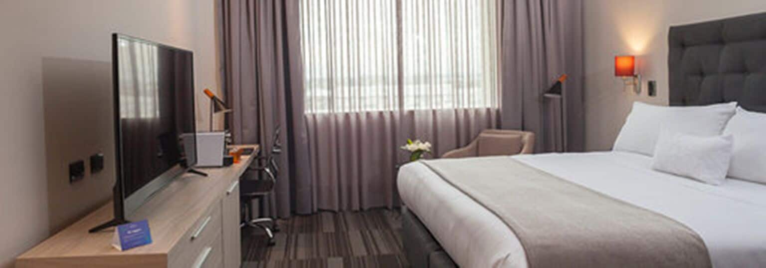 A hotel room with a bed, a desk with a computer, a chair, and a TV.
