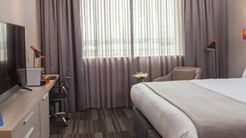 A hotel room with a bed, a desk with a computer, a chair, and a TV.