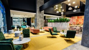 Un hall d’entrée moderne avec des sièges verts et orange, un sol en marbre et une grande plante décorative en guise de centre de table.