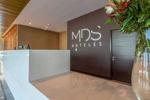 A reception area with a modern design, featuring a marble reception desk, a dark wall with the hotel name, and a large vase with flowers. - MDS Hotel Chillan (Chillan)