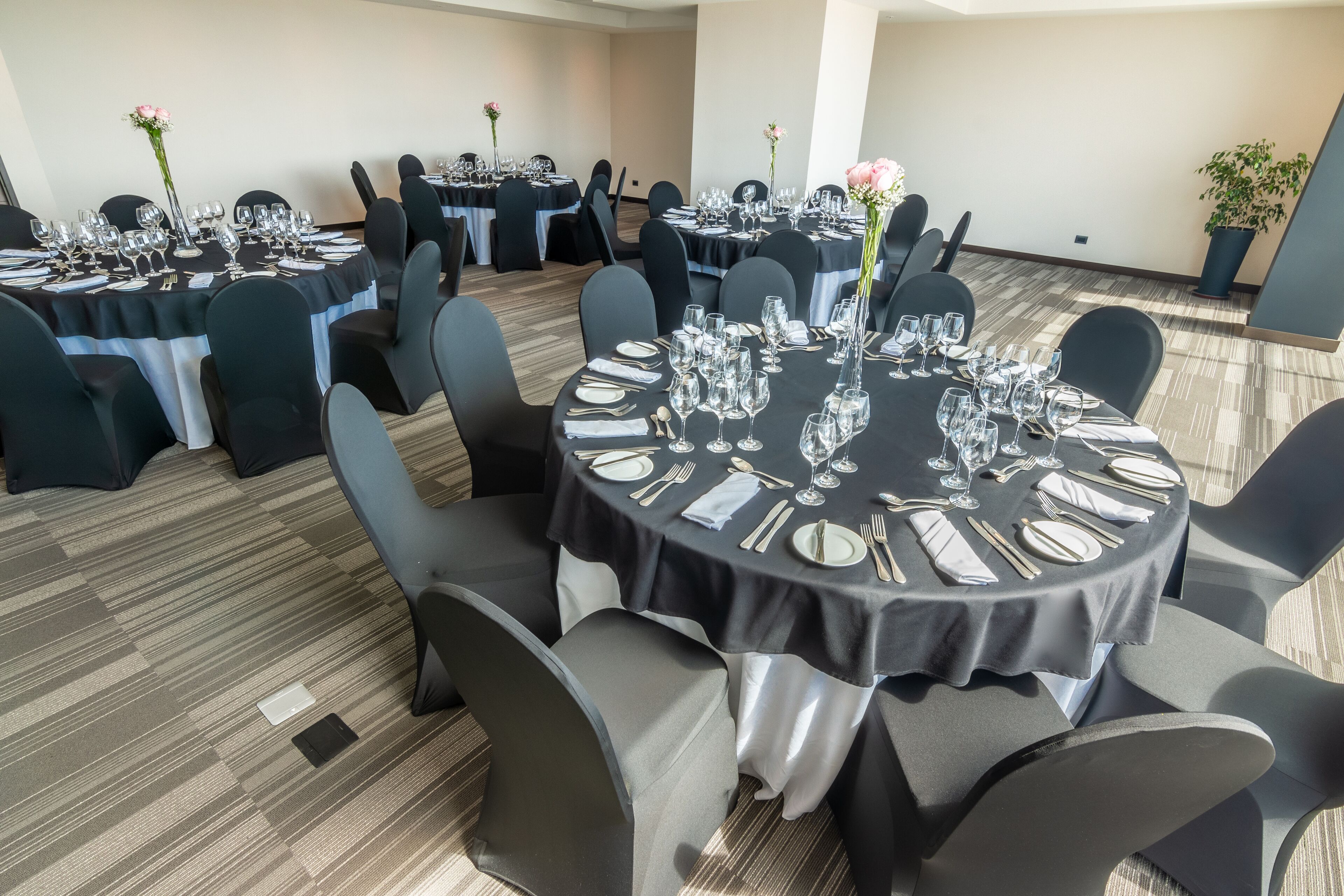 A conference room with round tables set for a formal event, featuring black tablecloths, white napkins, and silverware.