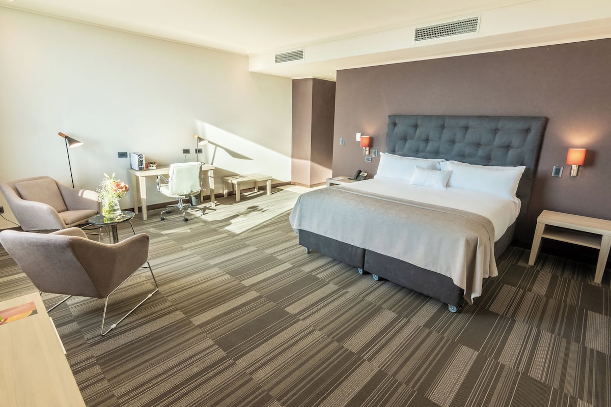 Ein modernes Hotelzimmer mit einem großen Bett, einem Schreibtisch, einem Stuhl und einem kleinen Tisch mit Blumen in einer Vase.