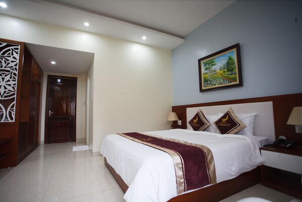 Una habitación de hotel con una cama grande, una mesita de noche, un cuadro en la pared y un armario de madera.