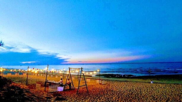 Una playa con un columpio y una fila de luces a lo largo de la orilla.