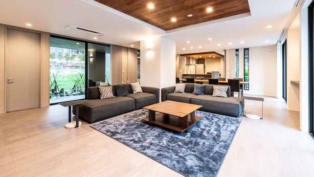 A modern living room with a sectional sofa, a coffee table, and a large window offering a view of greenery. - Towa Pure Cottages (Nasu)