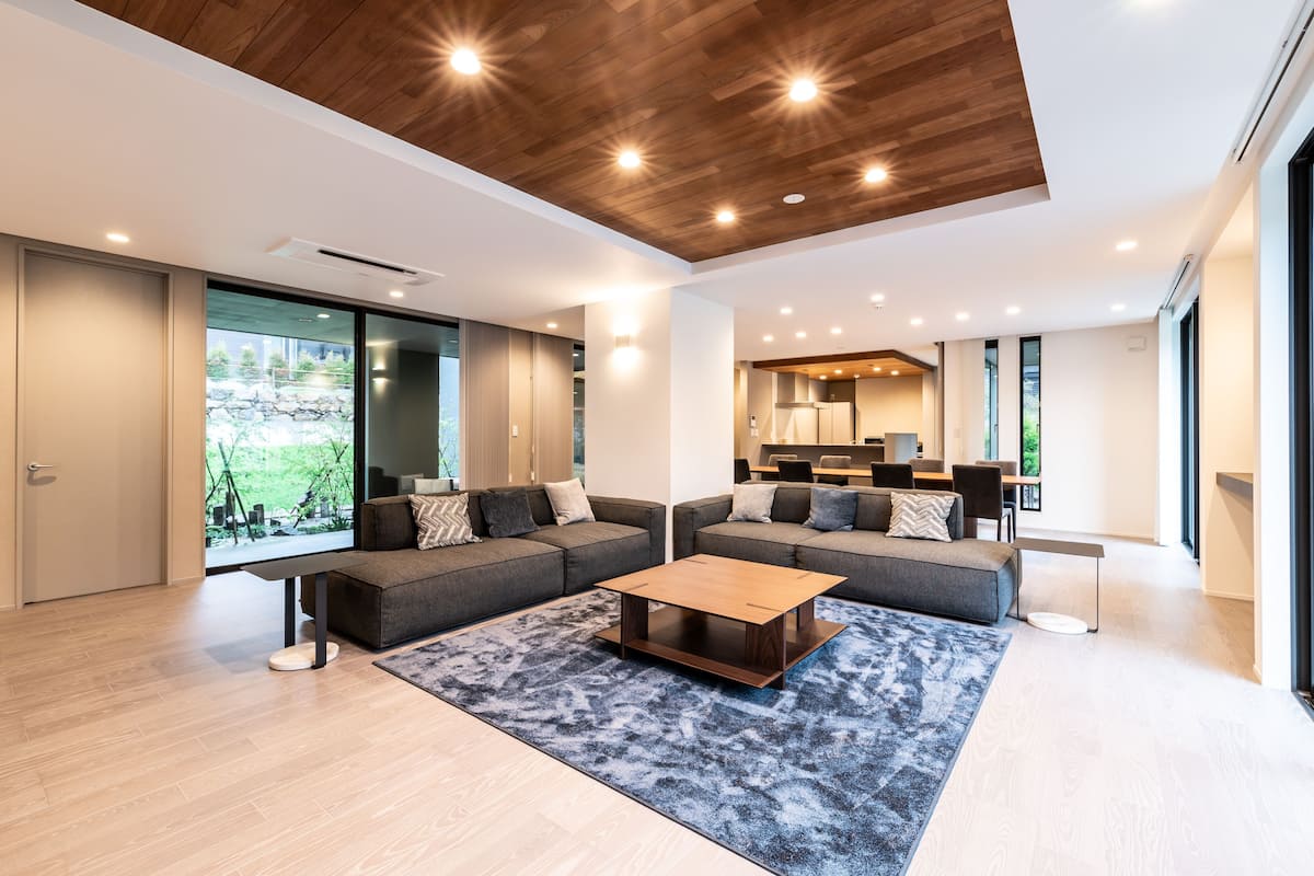 A modern living room with a sectional sofa, a coffee table, and a large window offering a view of greenery.