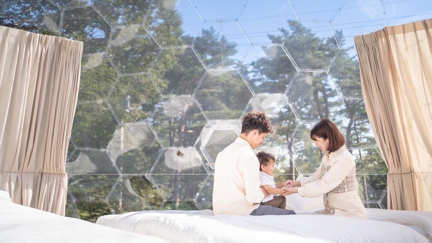 A room with a large window, a bed, and a geometric glass structure outside.