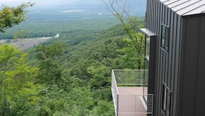 A modern building with a balcony overlooking a dense forest and distant mountains. - Towa Pure Cottages (Nasu)
