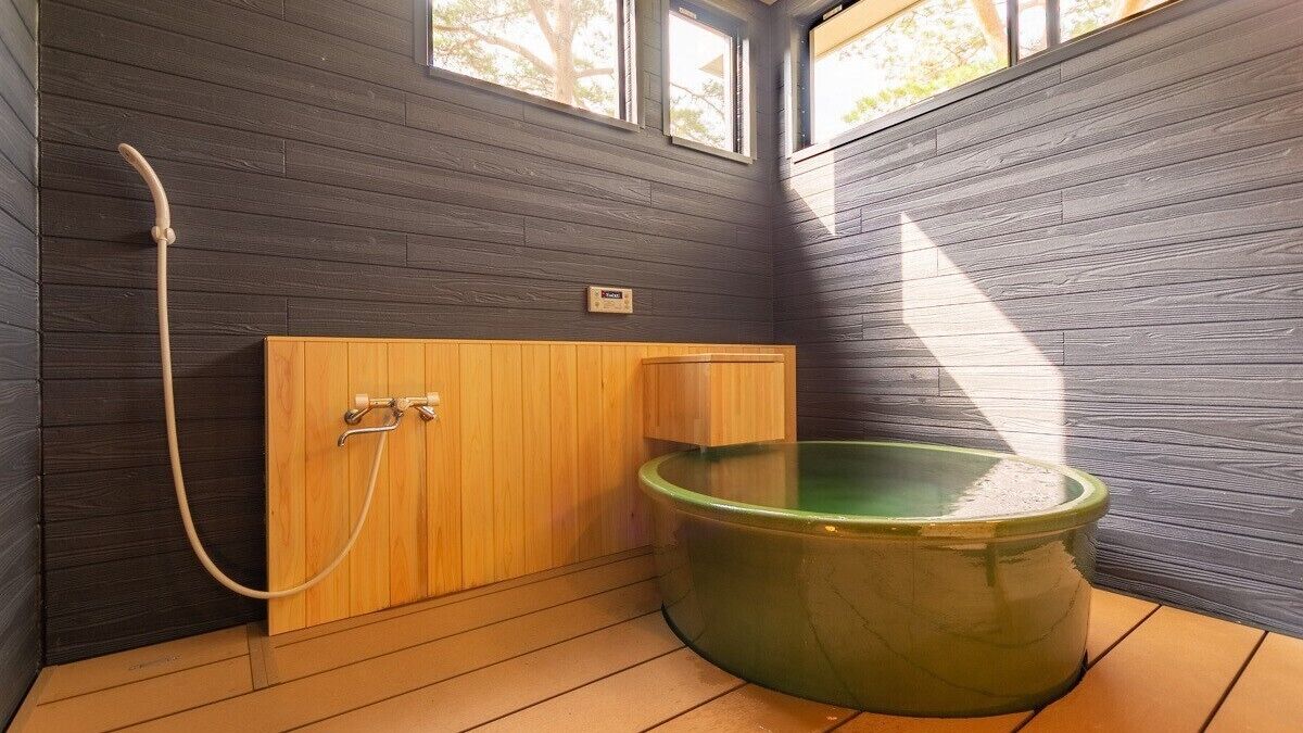 A wooden sauna with a green tub, a wooden bench, and a hose.