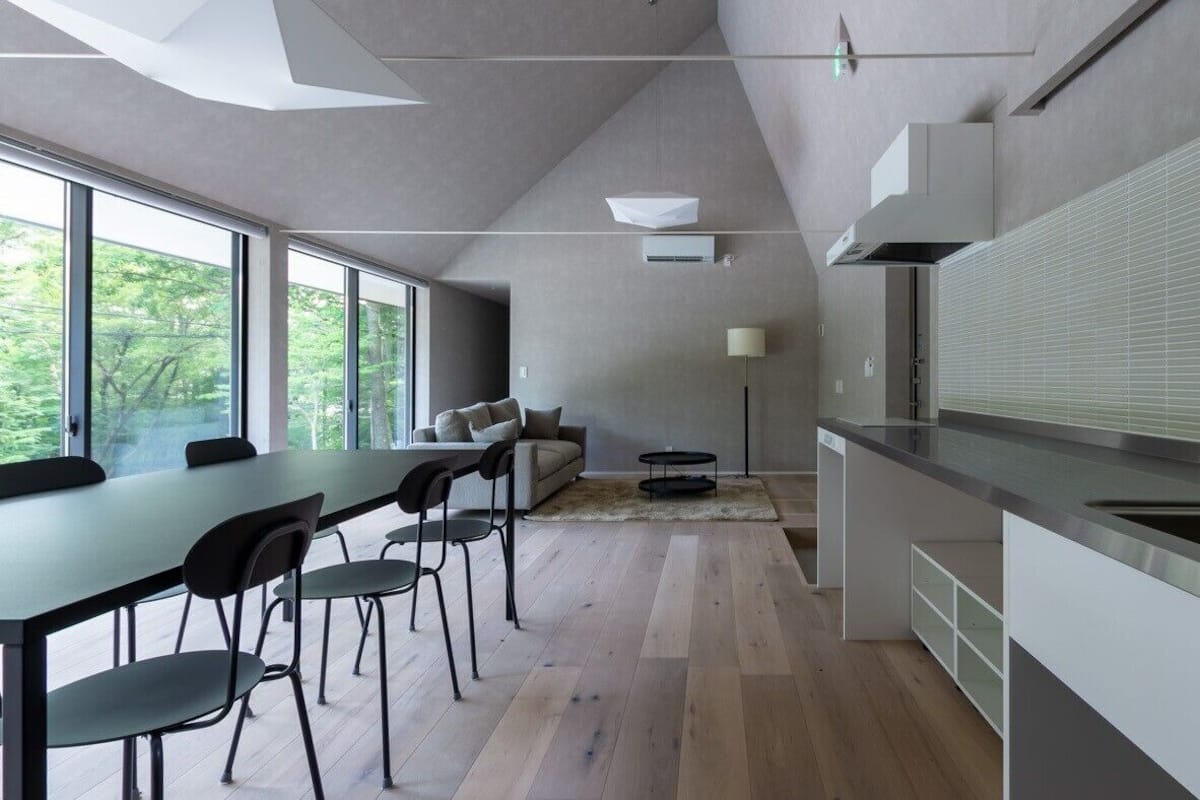 A modern kitchen with a dining area, large windows, and a view of trees.