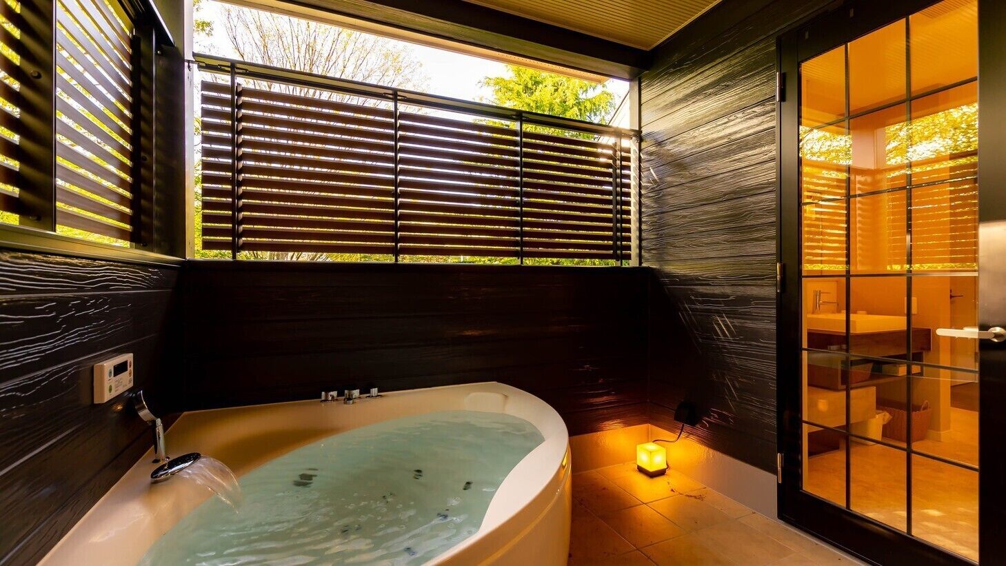 A modern bathroom with a freestanding bathtub, a glass shower enclosure, and a view of the outdoors through large windows.