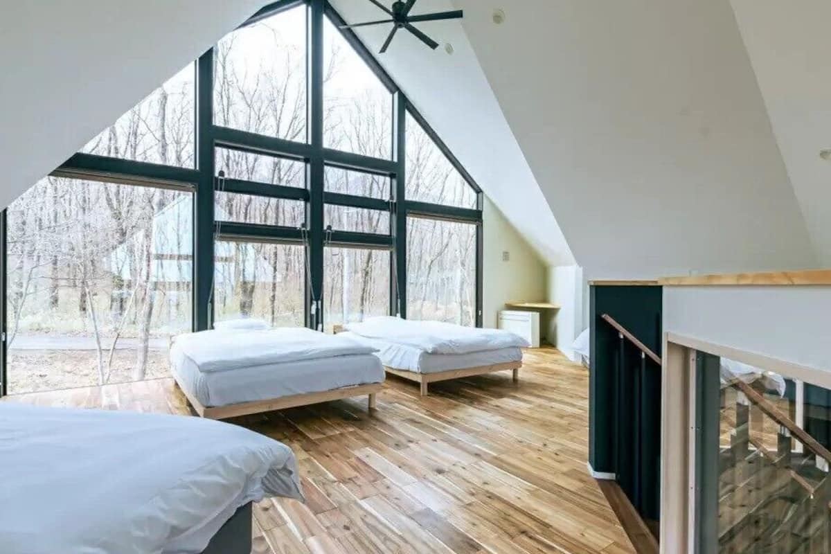 A high-ceilinged room with large windows, two beds, and a wooden floor.