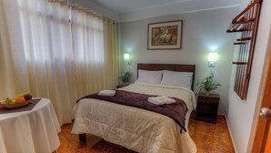 Une chambre bien rangée, avec un lit, une petite table sur laquelle sont disposés des fruits et un tableau accroché au mur.