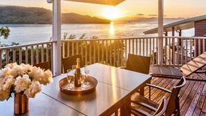 Eine Holzterrasse mit Tisch für zwei Personen, mit Blick auf ein Gewässer bei Sonnenuntergang.