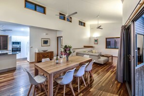 A modern kitchen with built-in appliances, a dining area with a wooden table and white chairs, and a living area with a sofa and a coffee table. - Casuarina Cove 12, Stunning Sea View Apartment on Hamilton Island (Hamilton Island)