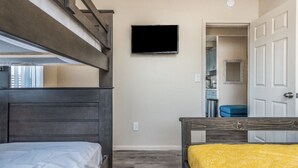 Ein Schlafzimmer mit Etagenbetten, einem an der Wand befestigten Fernseher und einer Tür zu einem Badezimmer.