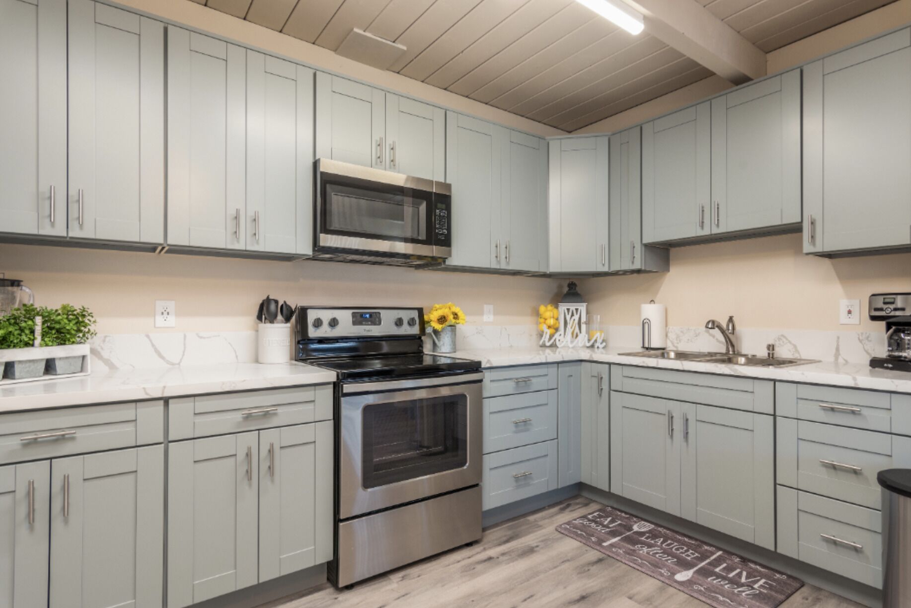 A modern kitchen with grey cabinets, stainless steel appliances, and a marble countertop.