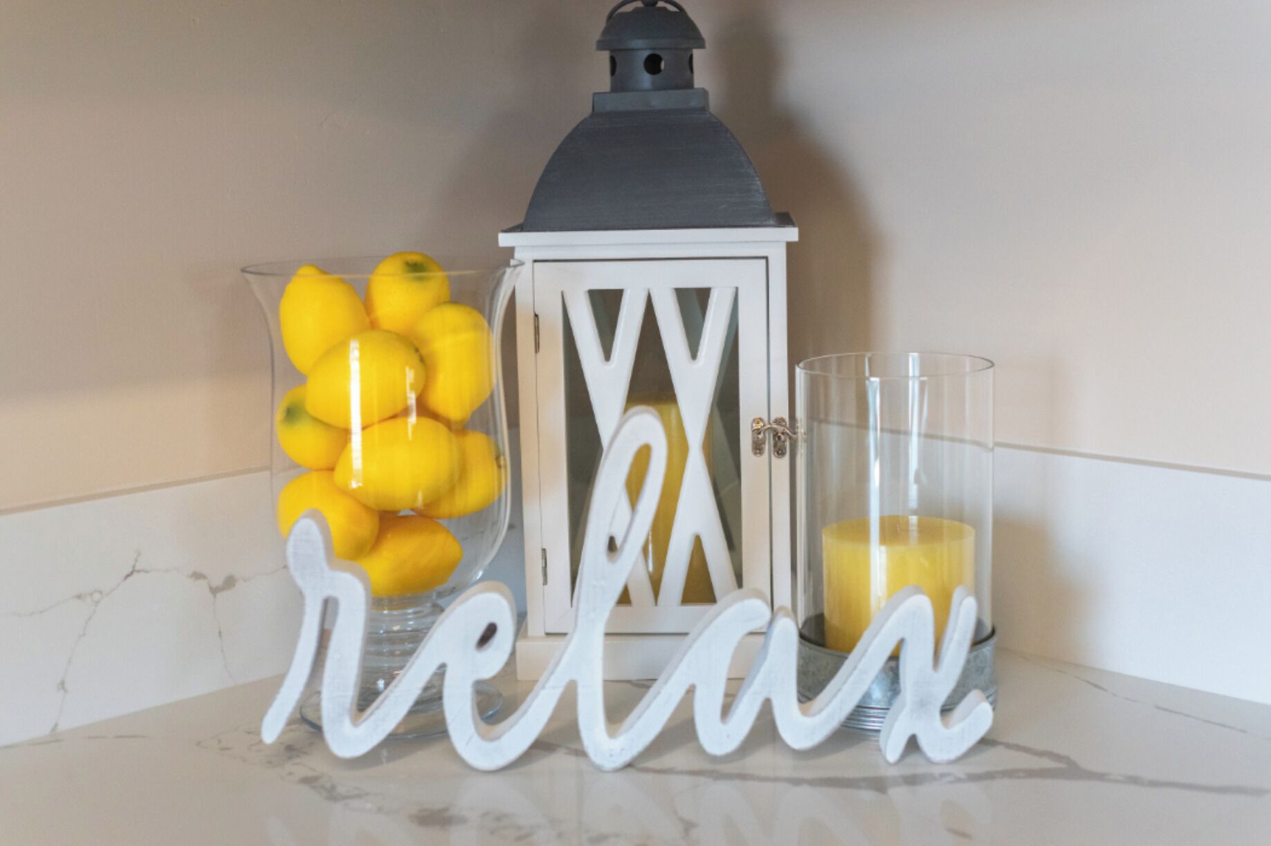 A white lantern, a glass container with lemons, and a glass with a yellow liquid, all placed on a marble surface.