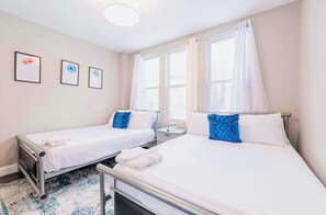 Une chambre d’hôtel avec deux lits simples, une petite table de chevet, une commode et une fenêtre avec des rideaux.