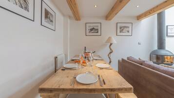 Une table de salle à manger en bois, mise avec des assiettes, des couverts et des verres, flanquée d’un canapé et d’une cheminée.