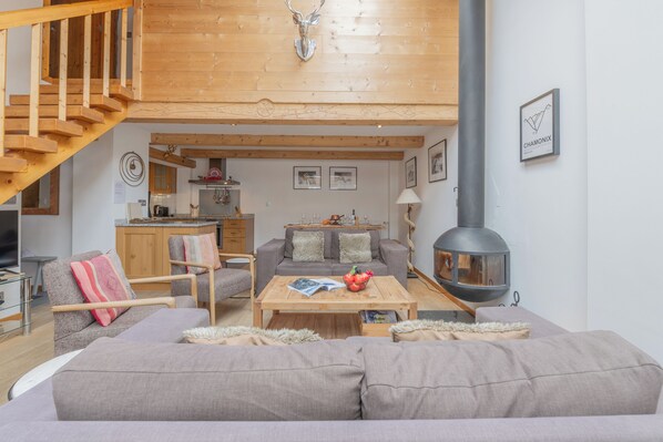 Una sala de estar acogedora con sofá, una mesa de centro y chimenea. Una escalera conduce a un nivel superior.