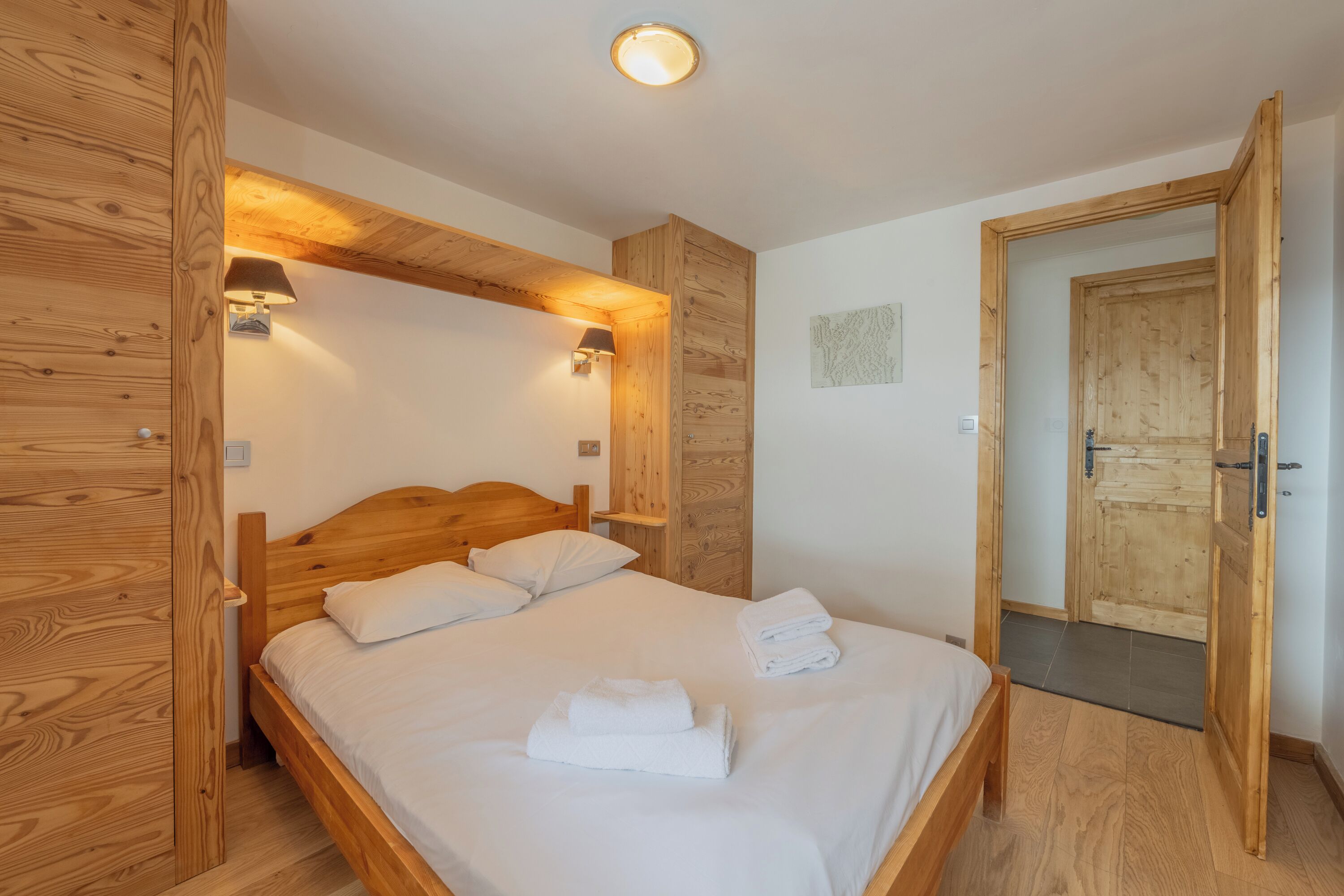 Une pièce avec un cadre en bois, comprenant un lit, deux lampes fixées au mur et une porte.