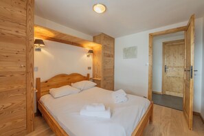 A wooden-framed room with a bed, two wall-mounted lamps, and a door. - Apt Clusettes 1-min walk to ski + parking & WiFi, Le Tour (Argentière), France (Le Tour (Argentière))