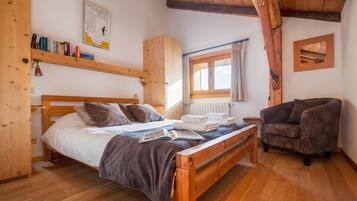Une pièce confortable avec un lit en bois, un coin lecture avec un fauteuil et une fenêtre avec des rideaux.