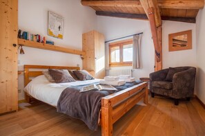 A cozy room with a wooden bed, a reading area with a chair, and a window with curtains.