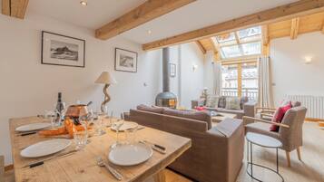 Un coin repas avec une table en bois dressée pour le repas, un canapé et une cheminée en arrière-plan.