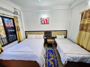 A hotel room with two beds, a window with a view, a painting on the wall, and a small table.