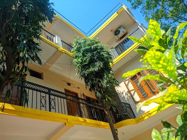 Un edificio de varios pisos con balcones, un árbol en el centro y un cielo azul despejado.