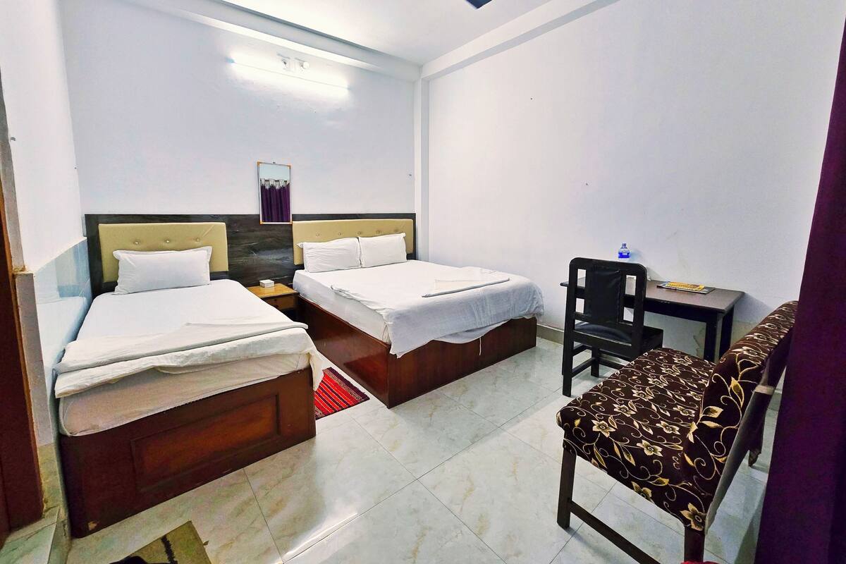A hotel room with two beds, a desk, a chair, a ceiling fan, and a water bottle on the desk.